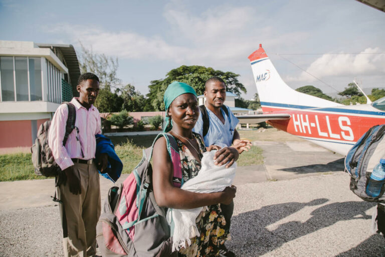 Mother cradles her malnourished infant and prepares to board MAF charity plane in Haiti.